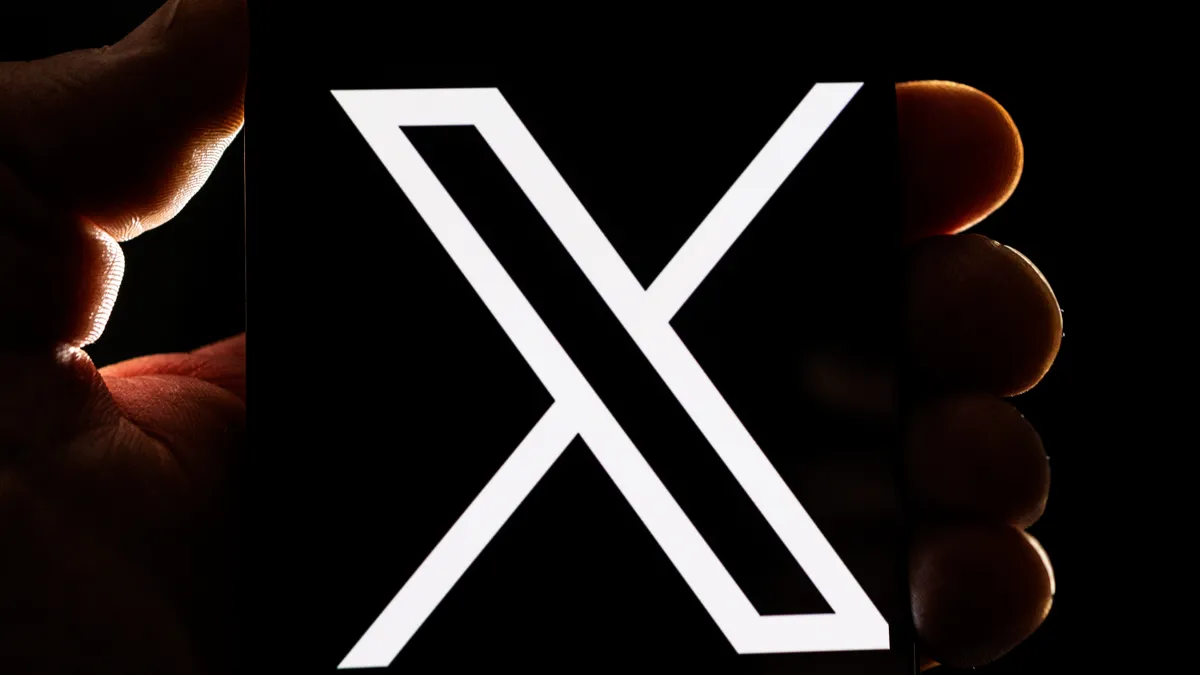 A human hand holding a black block displaying the letter "x"